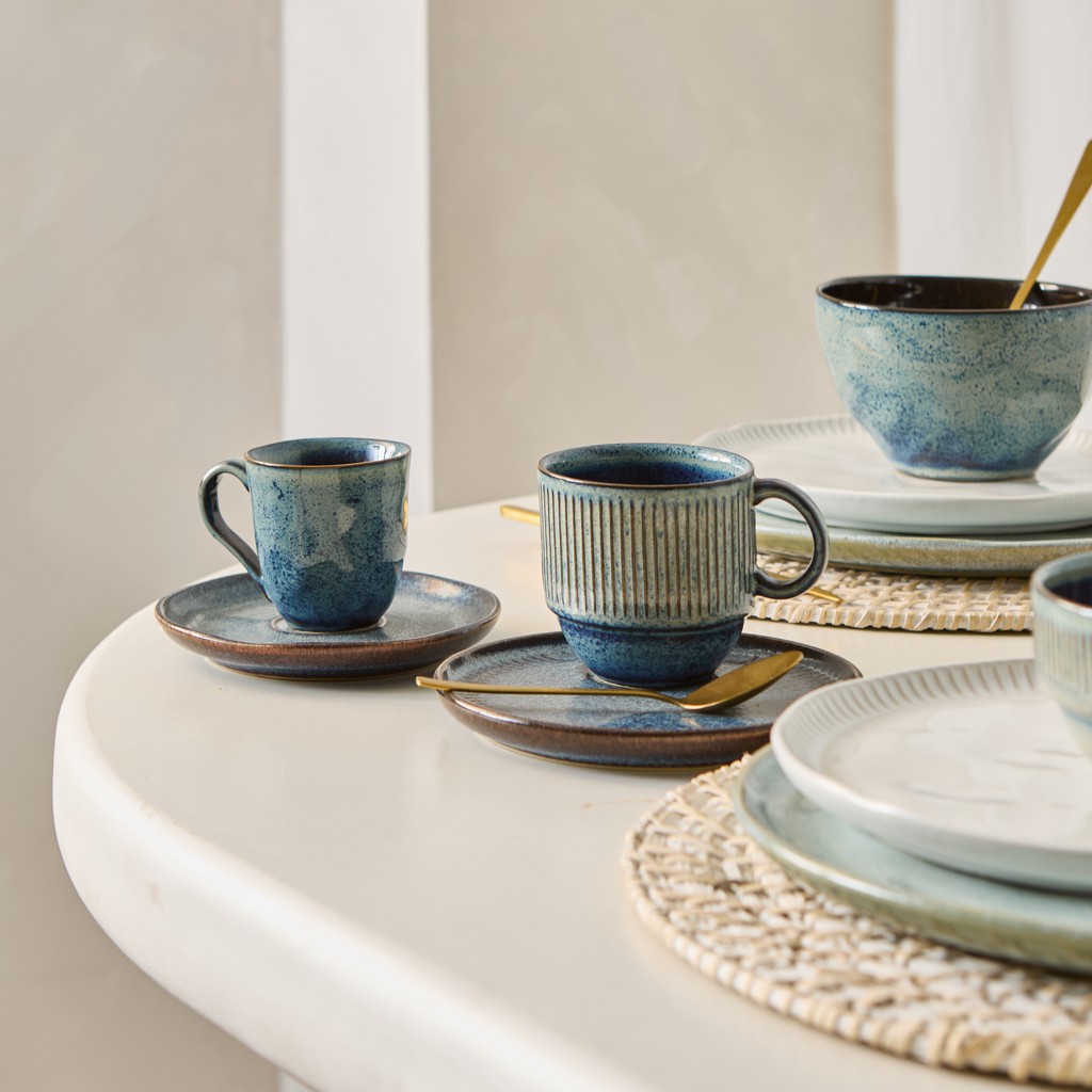 Tazas y platos de gres en tonos celestes combinados sobre una mesa puesta