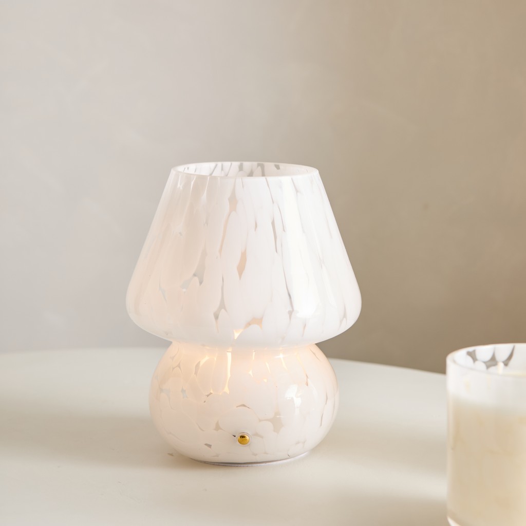 Portavelas de vidrio blanco jaspeado con velas encendidas sobre una mesa clara