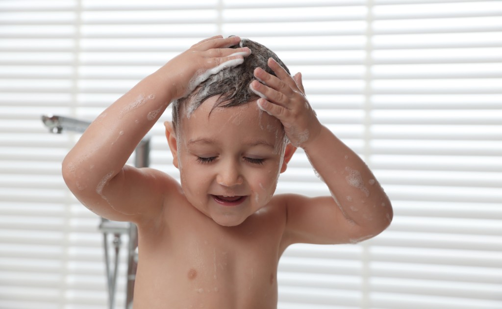 Criança aplicando condicionador no cabelo durante o banho