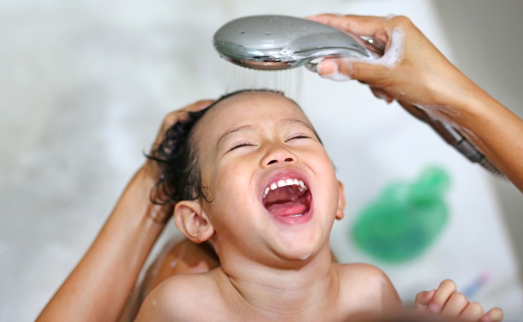 Cabelo infantil sendo enxaguado com ducha durante o banho