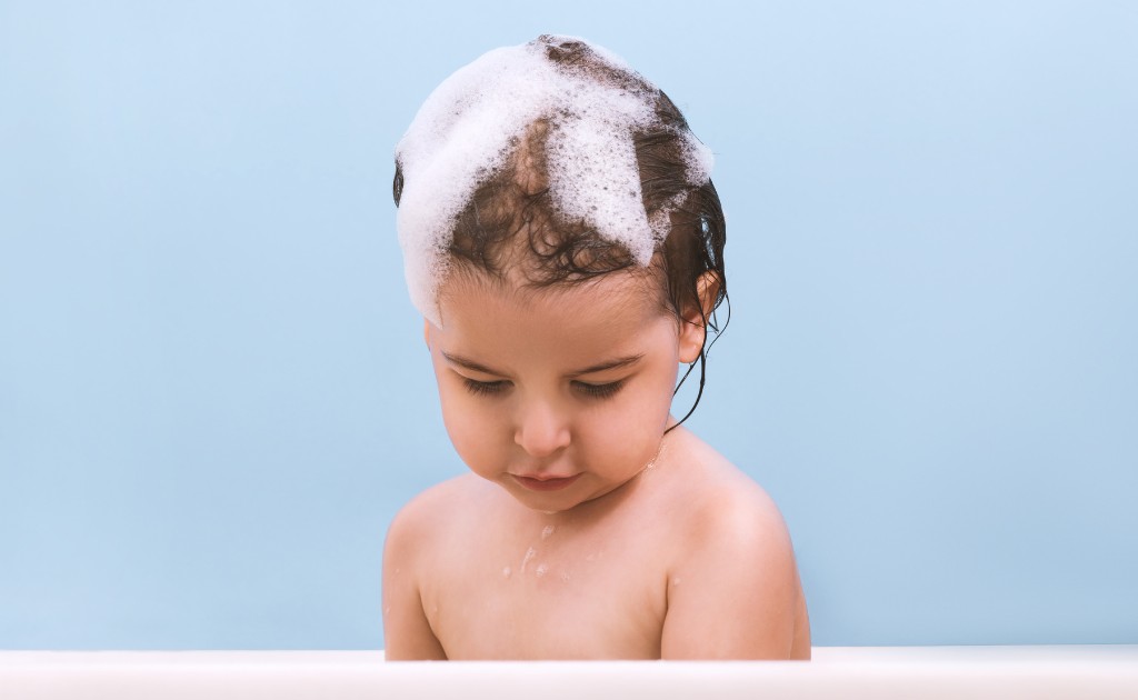 Criança com cabelo ensaboado em rotina de banho infantil