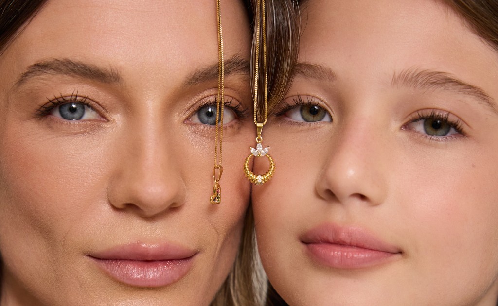 Uma mulher de olhos azuis e uma menina de olhos verdes olhando para a c&acirc;menra em segundo plano e um colar entre as duas no primeiro plano como objeto de foco.