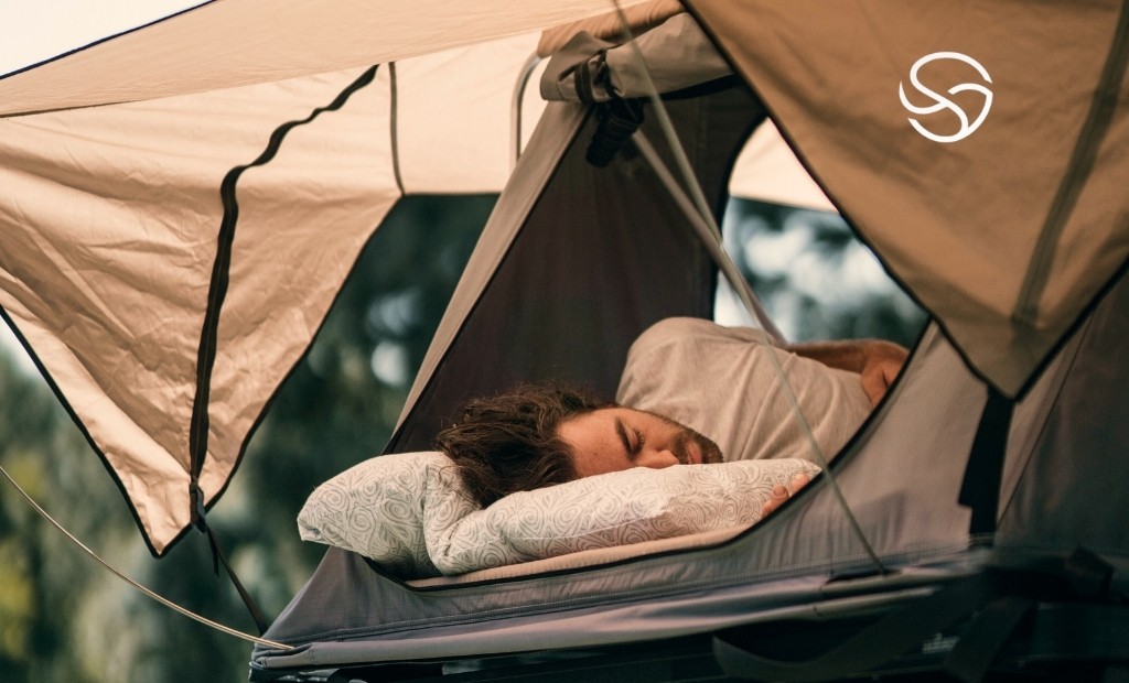 Homem dormindo confortavelmente em barraca de camping moderna com colchão inflável e travesseiro, representando camping inteligente e conforto na natureza.