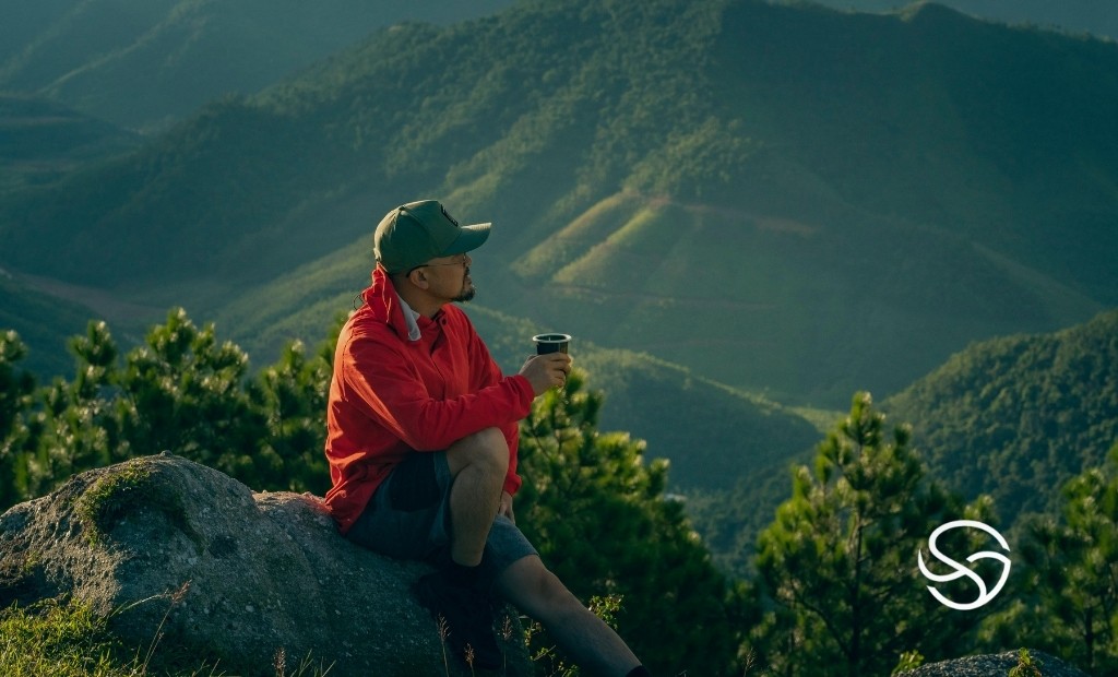 Campista descansando nas montanhas com caneca t&eacute;rmica, simbolizando autonomia, conforto e vida outdoor na natureza brasileira.