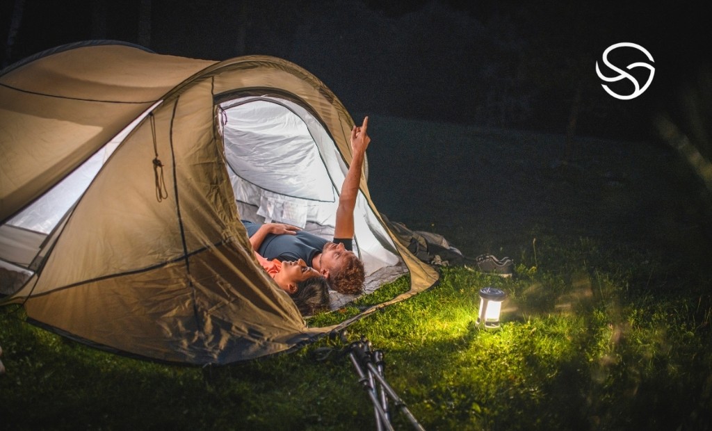 Área de camping iluminada por lanterna portátil com barraca montada em ambiente natural à noite