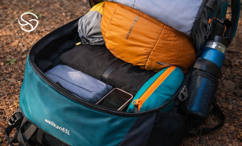 Mochila de trilha aberta com equipamentos de camping organizados em ambiente outdoor na natureza