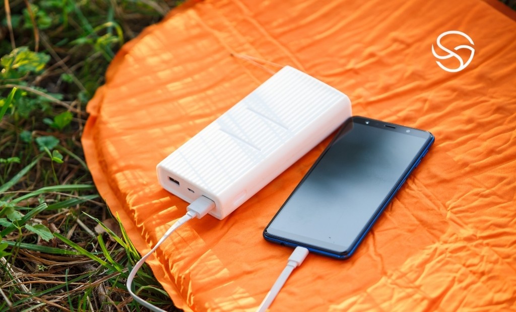 Pessoa carregando celular com powerbank portátil durante trilha em ambiente natural