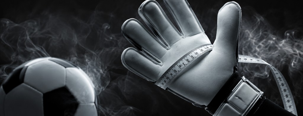 Guantes de portero con una cinta metrica y un balon para hacer referencia a como elegir la talla correcta de guantes.