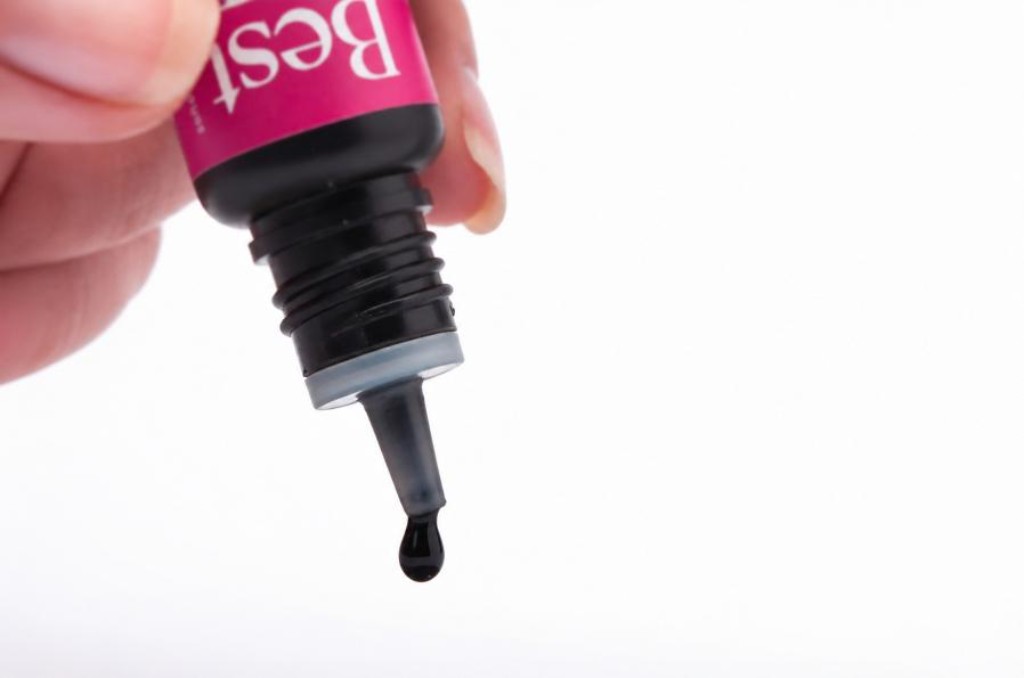 Gota de cola para extensão de cílios saindo do frasco de adesivo profissional.