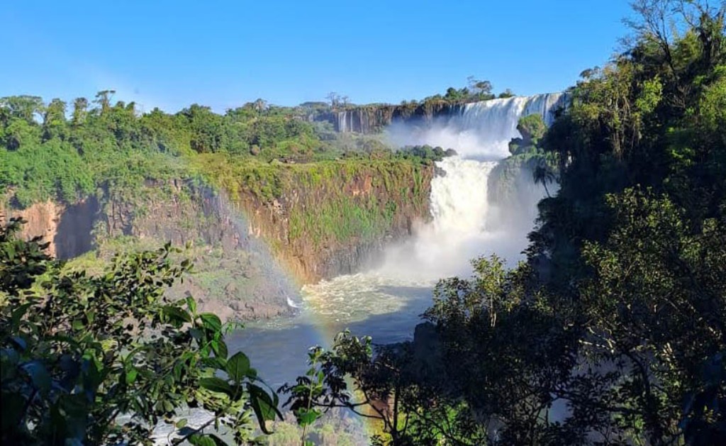 Paisaje natural de las Cataratas del Iguaz&uacute; en la selva de Misiones, Argentina, destacando un majestuoso salto de agua de dos niveles enmarcado por &aacute;rboles nativos y un arco&iacute;ris n&iacute;tido y colorido cruzando el ca&ntilde;&oacute;n