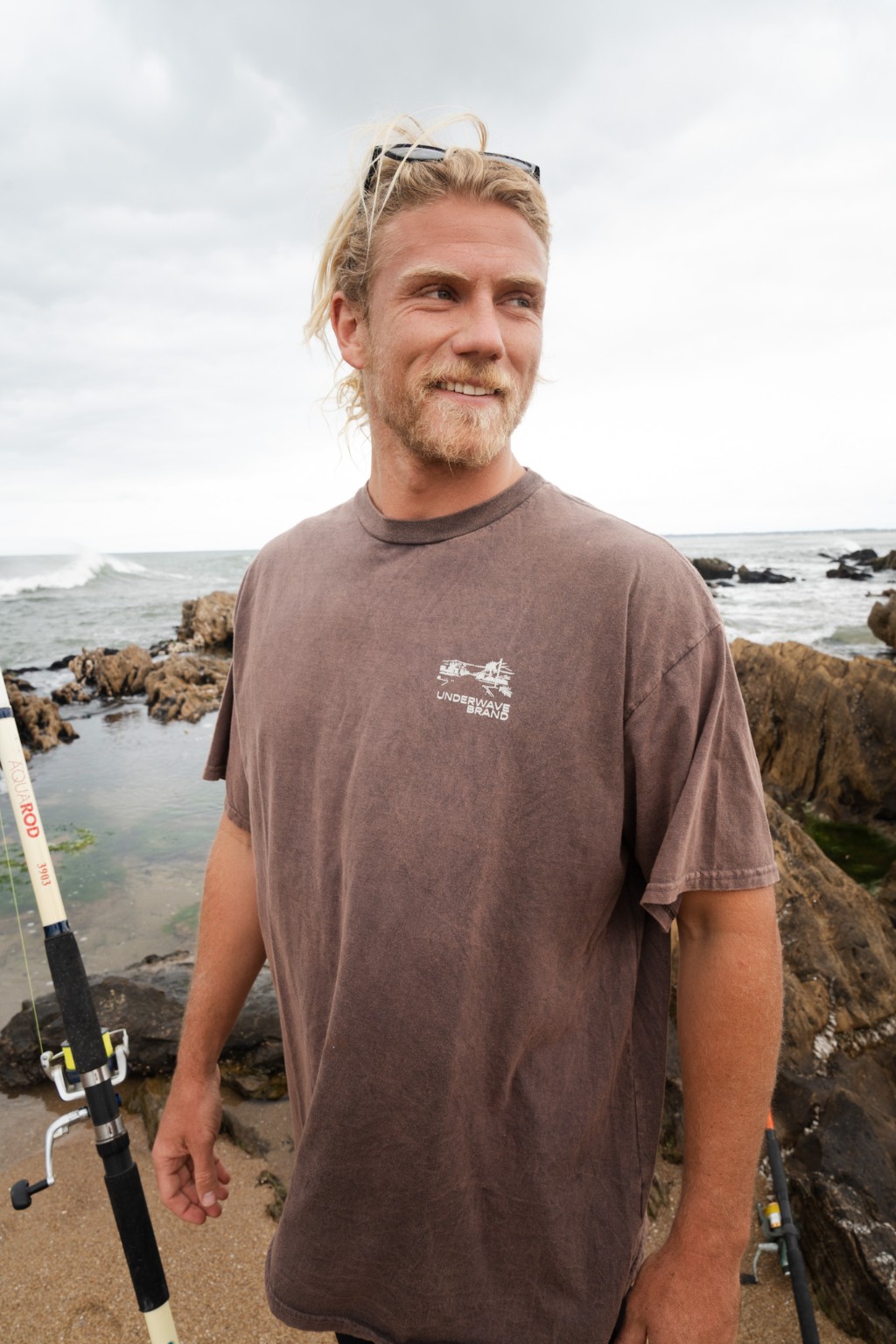 Chuck con una ca&ntilde;a de pescar y remera de Underwave en la costa de La Pedrera