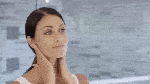 mulher passando creme no rosto em um cenário azulado.