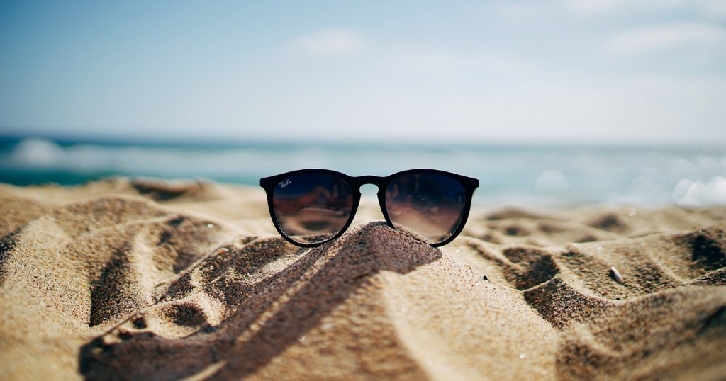 óculos de praia na areia com fundo do mar